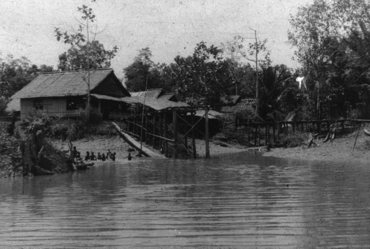 BD/216/16 -
Huizen aan de oever van een rivier met spelende kinderen