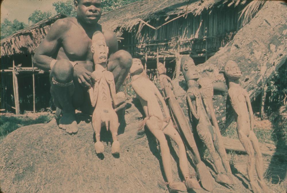 BD/30/26 - 
Man and ancestor statues in front of two men&#039;s houses
