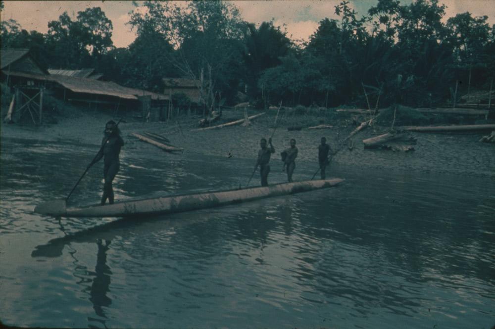 BD/30/3 -
Asmat men in a prow on the river in front of a settlement of stilt houses