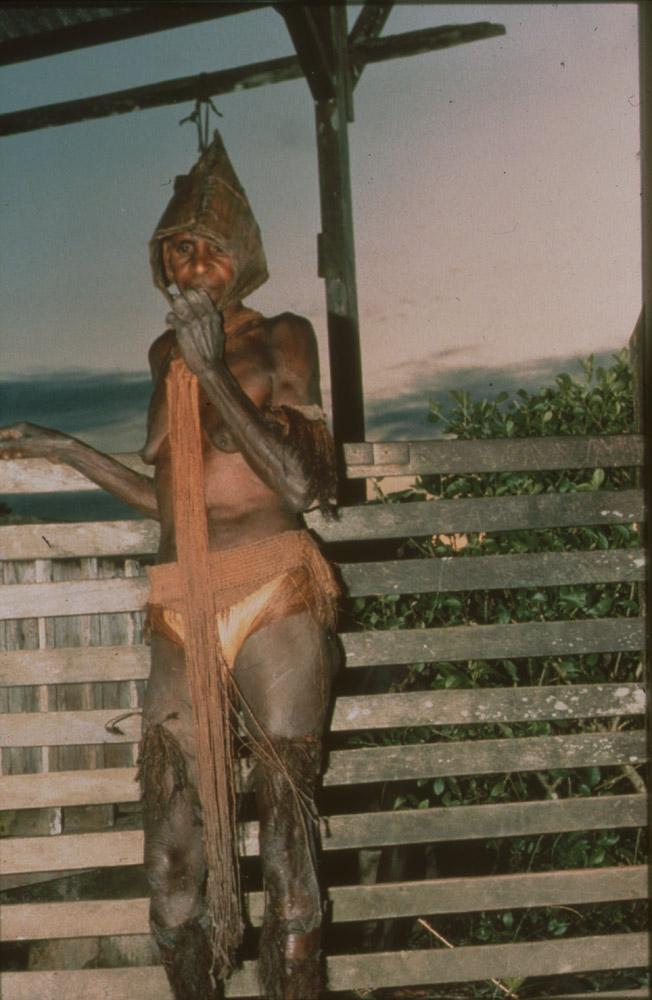 BD/30/75 - 
Asmat widow in mourning cloths standing on veranda
