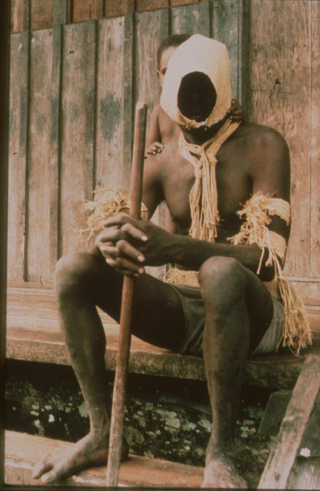 BD/30/76 -
Asmat man in mourning cloths sitting on stairs with a child behind him
