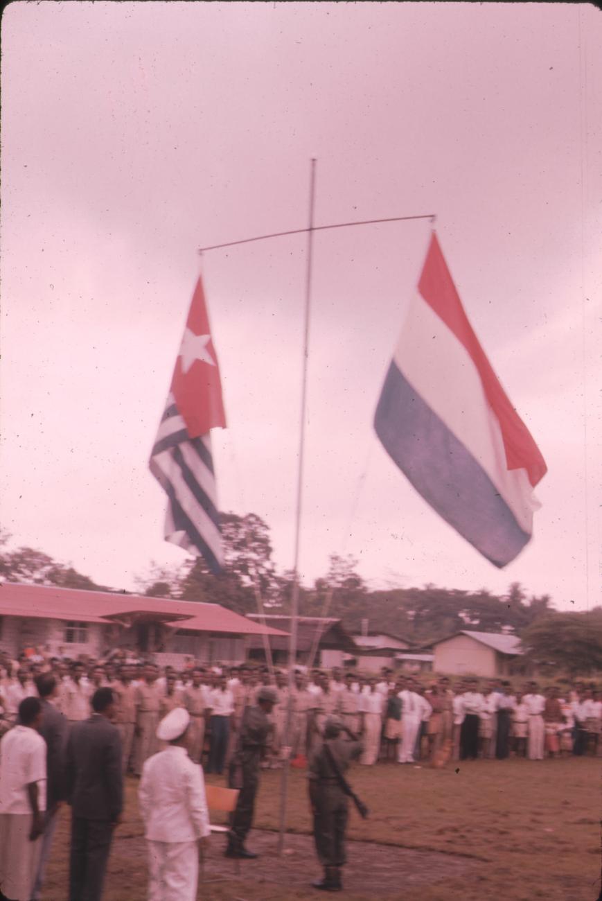 BD/171/25 -
Festiviteit, vlaggenmast met Nederlandse vlag en Papoeavlag.