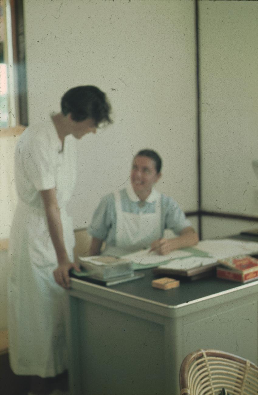 BD/171/597 -
Twee verpleegsters bij een bureau.