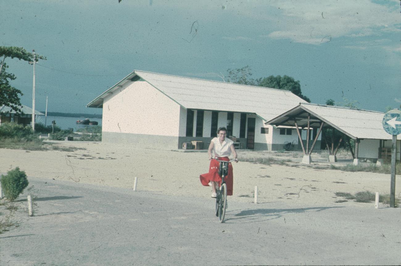 BD/171/667 -
Westerse vrouw op fiets, gebouwen op achtergrond.